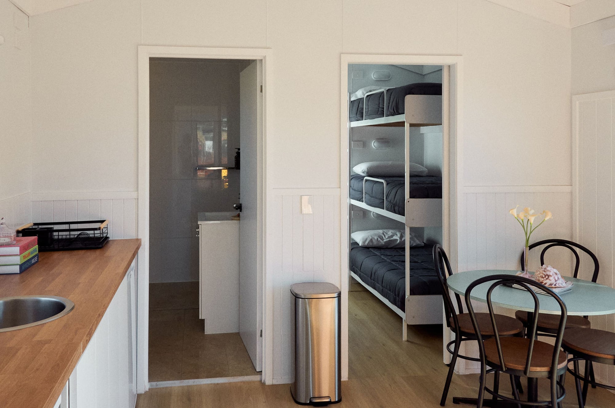 Modern kitchenette and an open doorway revealing bunk beds in Yerriyong B Cabin.